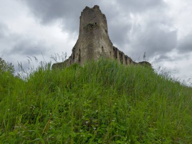 17. yüzyılın kuzey taş gözlem kulesi Sydoriv Şatosu, Ukrayna, yağmurlu bir günde bulutlu gökyüzüne karşı ön planda çimlerle kaplı tepe yamaçlı