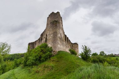 17. yüzyılın harap Sydoriv Kalesi 'nin kuzeyindeki Sydoriv köyü, Ukrayna' daki taş gözetleme kulesi yağmurlu bir günde ön planda çimlerle kaplanmış tepe manzaralı.
