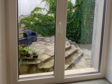 Pencerenin içinden bitişik asfalt verandaya birkaç adımla ve bulutlu bir günde tırmanma bitkileriyle kaplı karşı duvarla bak.