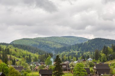 Dağ sırtları köknar ve yaprak döken ormanlarla kaplı bulutlu gökyüzüne karşı vadide bir dağ köyü var bahar sabahı bulutlu bir ön planda.