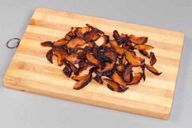 Bambu kesme tahtasındaki kuru erik dilimleri gri arka planda.