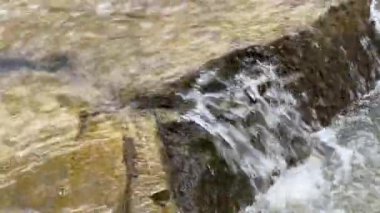 Mountain stream with rocky bank flowing into river close-up