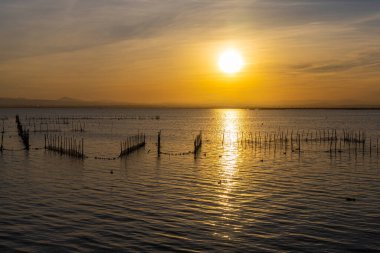 Balık ağları ve güneşli yollarla dolu göl turuncu bir günbatımının arka planına karşı