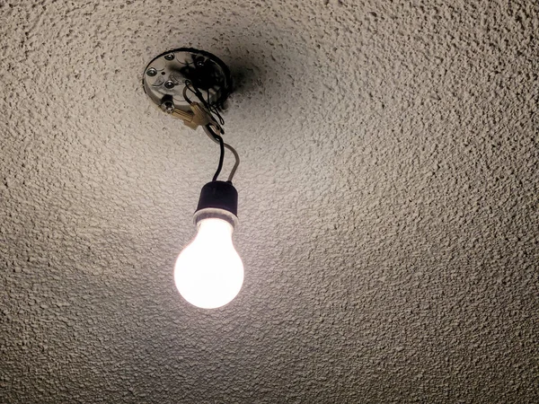 Glowing bare light bulb hanging from a light fixture on a popcorn ceiling
