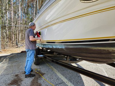 Bir sürat teknesinde portatif el cilası kullanan beyaz bir adam.