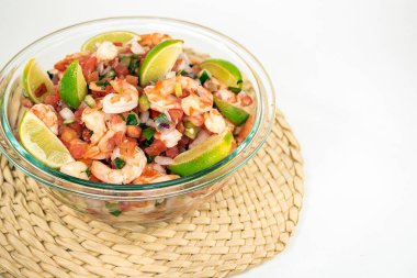 Fresh shrimp salad with lime slices in a glass bowl on a bamboo mat isolated on white 