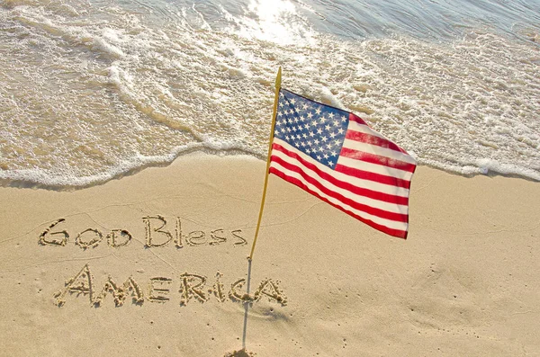 愿上帝保佑美国在沙滩上的文字 阳光下挂着美国国旗 — 图库照片