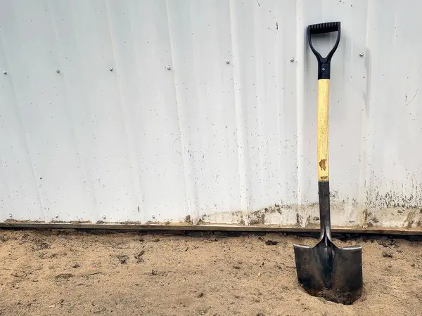 Single shovel leaning on metal siding stuck in dirt