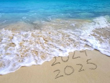 Dalgalar 2024 metni hafifçe siler ve 2025 'i plaj kumsalında açık mavi suyla bırakır.