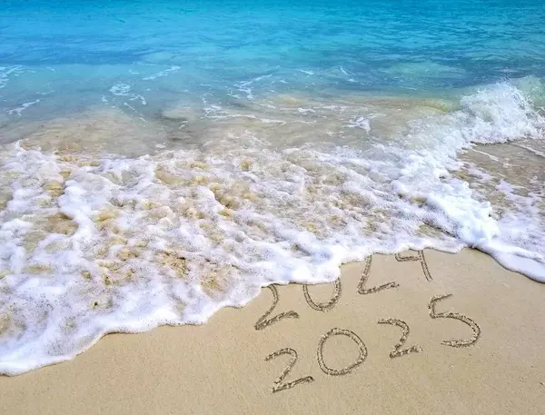 Dalgalar 2024 metni hafifçe siler ve 2025 'i plaj kumsalında açık mavi suyla bırakır.
