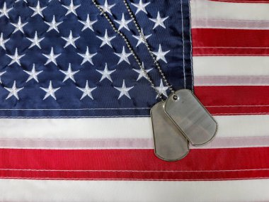 Amerikan bayrağının üzerinde duran künyeler vatanseverliği ve fedakarlığı simgeliyor.