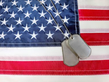 Künyeler Amerikan bayrağının bir bölümünde duruyor. Yıldızları ve çizgileri ayrıntılı bir şekilde gösteriyor. Metal etiketler kumaşa karşı, askerlik ve vatanseverliği simgeliyor.