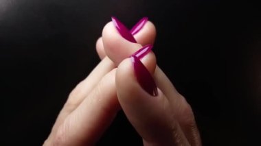 Tırnak sanatı. Siyah arka planda ideal mor jel cilası manikürü. El kol hareketi yapan kadın parmakları. Güzel tırnaklar, el derisi kavramı.