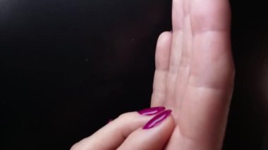 Manikür ve manikür. Kadın parmaklarının yavaşça birbirine dokunması ve aşağı yukarı kayması. Siyah arka planda zarif manikürlü tırnakları olan kadın elleri. Parlak mor tırnak cilası. Güzel tırnaklar, el derisi konsepti.