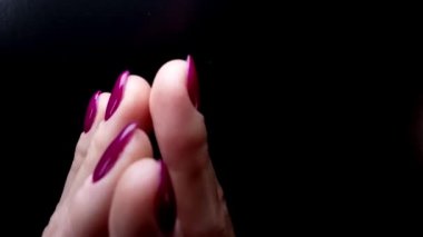 Tırnak sanatı ve manikür yaratıcı video. Mor jöle ojeli ve parlak kauçuk paltoyla boyanmış ideal zarif kadın tırnakları. Pürüzsüz, yavaş çekim ve kadının parmaklarının siyah arka plana değmesi.