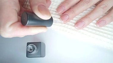 Jel cilası manikür, adım adım video eğitimi. 7. adım Nails astarı. Bir kadın yakın çekimde tırnaklarına oje sürerken görülüyor.