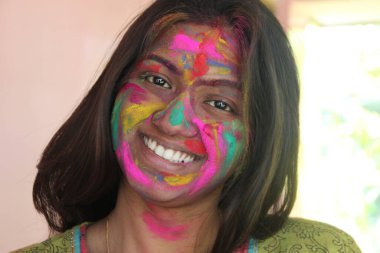 Yüzü canlı renklerle dolu, kameraya doğru bakan ve gülümseyen Holi konsepti olan 30 'lu yaşlarda Hintli bir kadın.