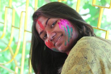 Yüzü canlı renklerle dolu, kameraya doğru bakan ve gülümseyen Holi konsepti olan 30 'lu yaşlarda Hintli bir kadın.