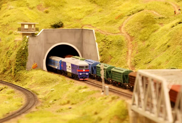 A locomotive with wagons leaves the tunnel. Landscape layout with railroad, cars, residential and industrial buildings. Monuments of architecture and sights. Hobbies of building miniatures