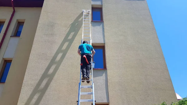一个在高处洗窗的工人爬上梯子爬上房屋的墙壁 高层清洁立面的工作 从事危险工作的人 — 图库照片