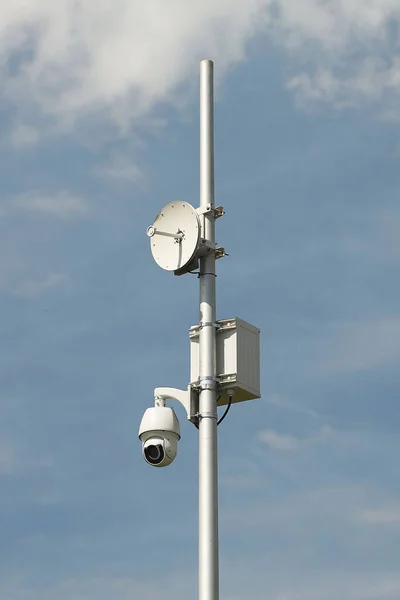 Surveillance system with an orange warning light located on a pole in the open. The threat of privacy and the protection of personal data. Security tracking on the streets of the city. Human mass.