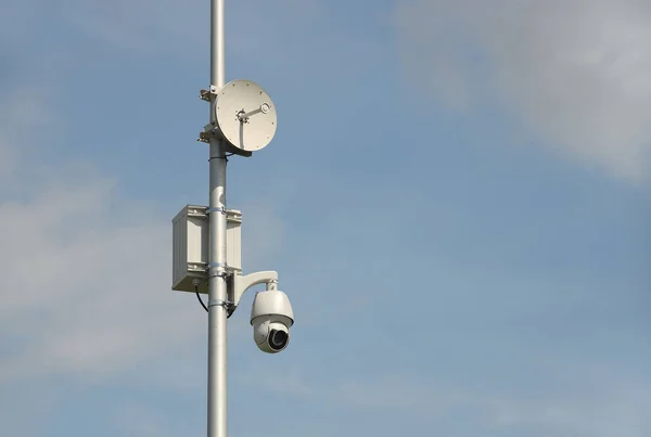 Surveillance system with an orange warning light located on a pole in the open. The threat of privacy and the protection of personal data. Security tracking on the streets of the city. Human mass.