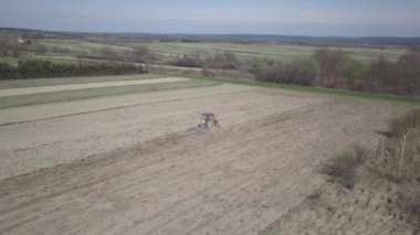Bir çiftçi bir sembol ile kırmızı bir traktör tahıl köyü alan özel bir alanda sürülmüş topraklarda sows. Mekanizasyon bahar saha çalışması. Çiftçinin günlük yaşam. Toprak işleme. Tarım.