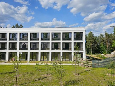 Design of the facade of a modern hotel-type building. A rectangular white architectural structure among a green forest. clipart