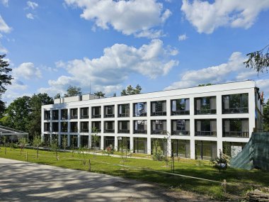 Modern otel tipi bir binanın ön cephesinin tasarımı. Yeşil bir orman arasında dikdörtgen beyaz bir mimari yapı..