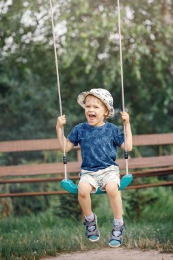Güzel bir yaz bahçesinde, sıcak ve güneşli bir günde salıncakta sallanan sevimli küçük bir çocuk. Çocuklar için aktif yaz tatili.