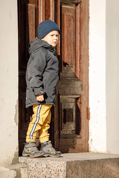 stock image A cute boy on an autumn day at the ancient door in the center of Klaipeda Old Town.