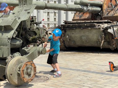 Ukrayna 'da savaş. Ukrayna 'nın başkenti Kyiv' de 17 Haziran 2022 'de imha edilmiş ağır silah parçalarıyla oynayan küçük çocuk.