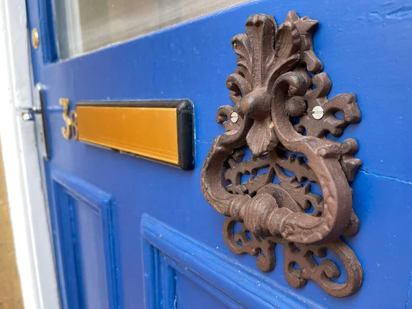 Close up of a heavy vintage door knocker on a blue door with golden mail slot