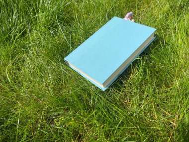 Açık havada yeşil çimlerde mavi ciltli kitap