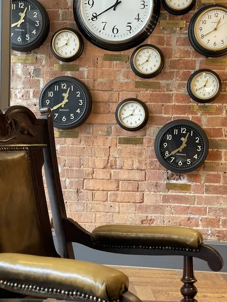 多くの時計で覆われたレンガの壁の近くのヴィンテージアームチェアの作物のショット — ストック写真