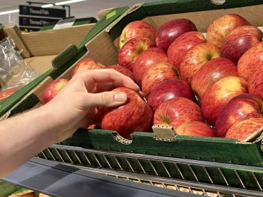 Süpermarketteki bir kutudan elma seçen tanınmayan bir müşterinin görüntüsü.