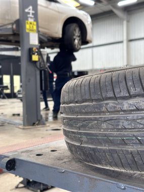 Araba lastiğinin dikey çekimi, tamirciler arka planda konuşuyor.