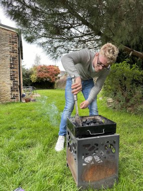 Genç ve yakışıklı bir adamın kömür ızgarasında ateş açarken dikey çekimi. Bahçe partisine hazırlanıyor.