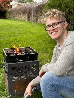 Bahçe partisi için ızgarayı hazırlarken kameraya gülümseyen neşeli genç adam.