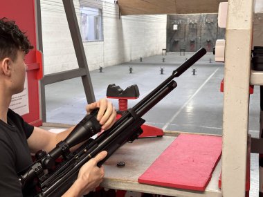 Atış poligonunda hava tüfeği ateşlemeye hazırlanan adam.