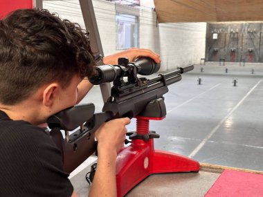 Optik kullanan, havalı tüfeğini atış poligonuna doğrultmuş bir adamın görüntüsü.
