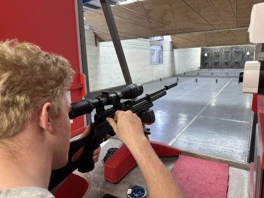 Menzilde ateş ederken tüfeğin dürbününe bakan adam.