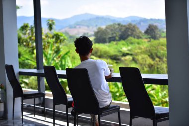 Asyalı adam dağları gören balkonda dinleniyor.