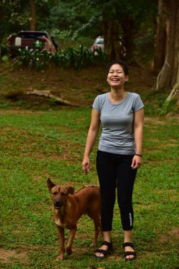 Asyalı bir kadın köpekle ormanda yürüyor. 