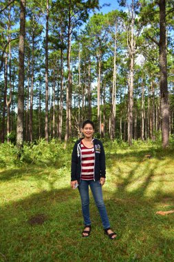 Gülümseyen Asyalı kadın çam ormanında poz veriyor 