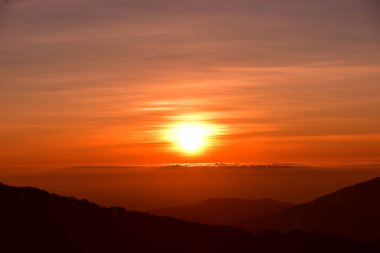 Gün doğumunda dağlarda güzel bir manzara. Bulutlu turuncu gökyüzü ve dağ sisi.