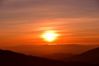 Gün doğumunda dağlarda güzel bir manzara. Bulutlu turuncu gökyüzü ve dağ sisi.