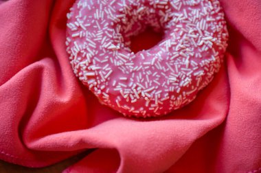 Beyaz parçacıklarla süslenmiş canlı pembe bir donut pelüş bir mercan kumaşa yerleştirilir. Bu enfes ikramınız sıcak ve davetkar bir atmosfer yaratıyor..