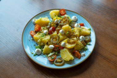 Baharatlı biber dilimli haşlanmış patates, taze vişneli domates ve doğranmış bahar soğanı, mavi tabakta canlı, aromalı bir tabak yapar..