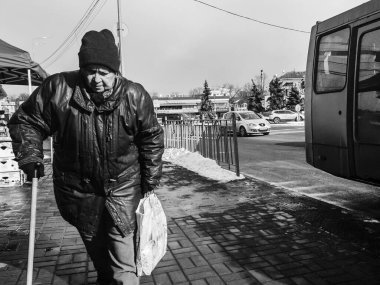 Kyiv, Ukrayna - 2 Mart 2025: Yaşlı bir adam kaldırımda yürürken, serin bir esinti hareketli şehri kasıp kavururken, elinde bir torba yiyecekle dikkatli bir şekilde yürür.